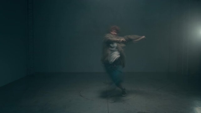 Front view wide angle shot of young man dancing dynamically under strobing lights in dark empty studio with accelerated motion blur effect, cinematic underground vibe, copy space