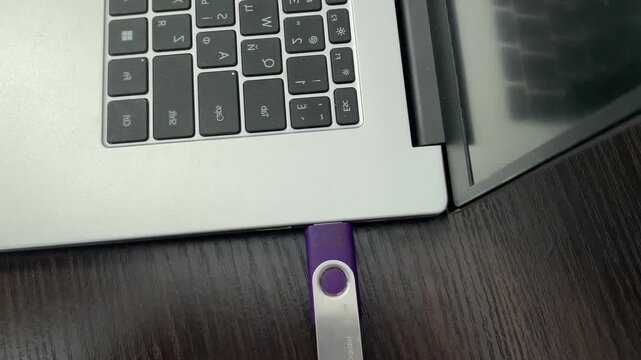 Attaching purple storage device to laptop port. Inserting portable flash drive into computer for file transfer. Connecting purple removable media device to laptop port for data transfer and backup