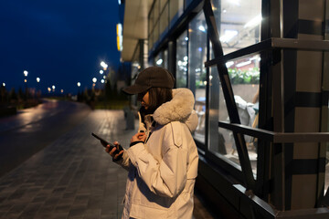 Woman stands outside a building at night looking at her phone near streetlights on the sidewalk © Mihail