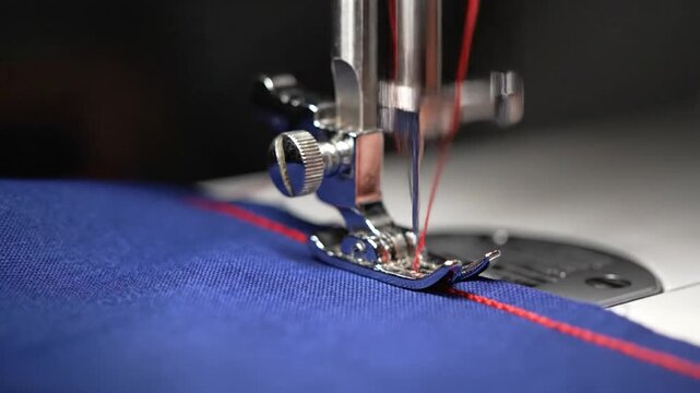 Sewing machine stitching red thread on blue fabric close-up.