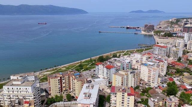 Aerial video of the urban waterfront in Vlora, Albania, showcasing a dense row of modern multi-story apartment complexes and the coastal boulevard. 