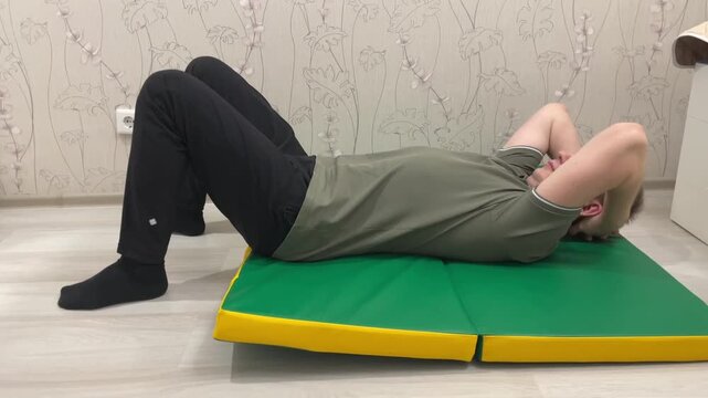 Male performing situps for strength. Adult male engaging in indoor abdominal strengthening routine. Individual practicing controlled core exercises on foldable green yellow mat indoors