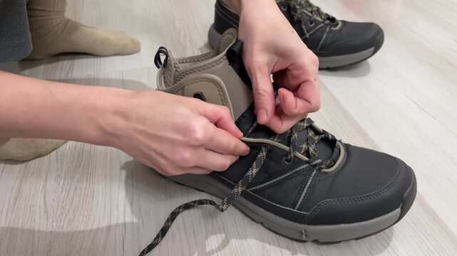 Boot fastening process. Preparing footwear by adjusting laces for optimal fit and comfort. Methodically tightening shoelaces on hiking boots to ensure safety and comfort during walking