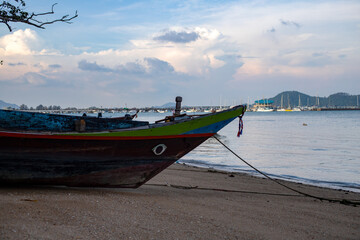 Traditional Thai longtail boat anchored on a quiet tropical beach with calm sea, distant islands and dramatic evening clouds. © Max