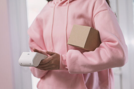 A close-up of a girl delivering parcels, a courier with a box and a wireless payment terminal, unrecognizable