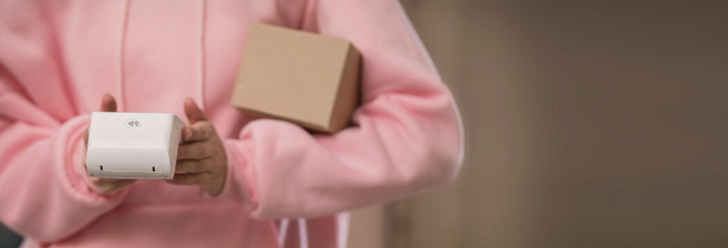 A close-up of a girl delivering parcels, a courier with a box and a wireless payment terminal, unrecognizable banner copy space