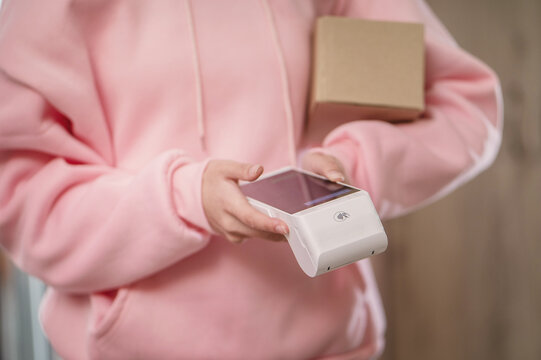 A close-up of a girl delivering parcels, a courier with a box and a wireless payment terminal, unrecognizable