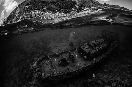 Dramatic over under split shot of a shipwreck off the coast of Curacao in black and white