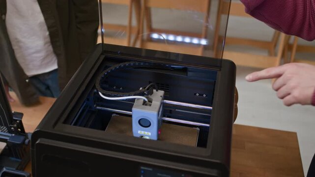 Tilt up shot of group of unrecognizable students together with their male teacher examining inner workings of 3D printer during class