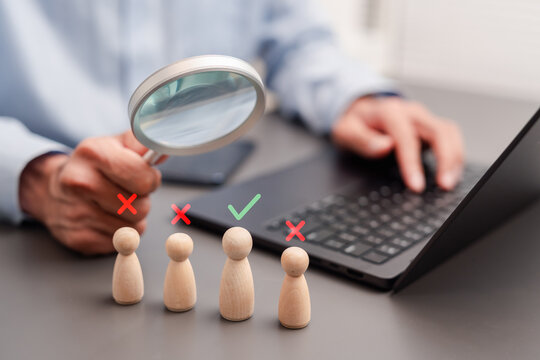 Human resources and recruitment concept for choosing candidate. Manager using magnifying glass to select the right employee from wooden figures.