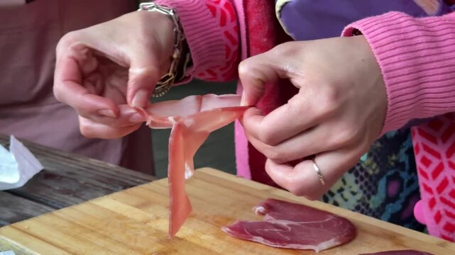 Thin jamon pieces carefully arranged by woman for sophisticated appetizer composition with rich meat texture and cozy dining atmosphere.