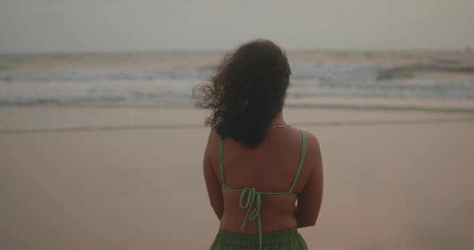 Woman standing on a beach, feeling the ocean breeze and warm sand, gazing at the breaking waves and distant horizon, embracing contemplation and personal space