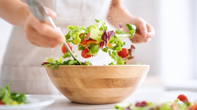Hands tossing a fresh green salad with cherry tomatoes in a wooden bowl