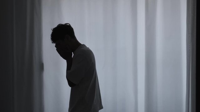 Emotional burnout in temporary rented apartment with silhouette man standing in front of window with closed curtains, minimal loneliness and copy space concept