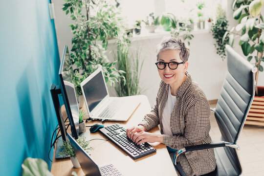 Smiling professional woman working on computer in bright modern office with plants and laptop