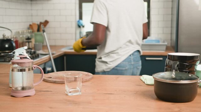 Adult Man in Yellow Gloves Organizes and Washes Dirty Dishes in a Bright Kitchen