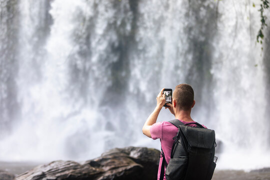 Tourist filming Phnom Kulen waterfall with mobile phone in Cambodia jungle. Smartphone video, travel blogging, technology and tropical vacation concept.