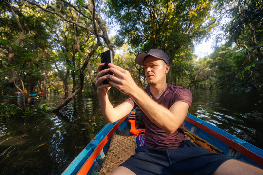 Tourist in boat taking photo with mobile phone of trees growing from water on Tonle Sap lake Cambodia. Eco tourism, travel photography, floating village and asian vacation concept.