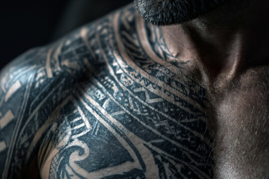 Dramatic close-up of a blackwork tribal tattoo covering a chest, bold solid ink patterns, strong contrast on skin, moody dark background