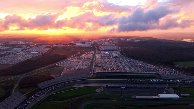 Drone view of thousands of new vehicles at a logistics hub during a dramatic sunset.