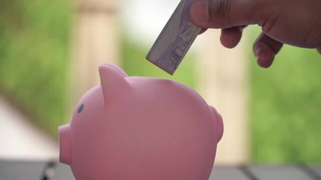 Close-up hand inserting coin into piggy bank, financial success and budgeting illustration. Personal finance concept with piggy bank and coins.