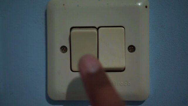 Finger pushing wall light switch, power on action, home lighting control, energy efficiency, closeup detail.