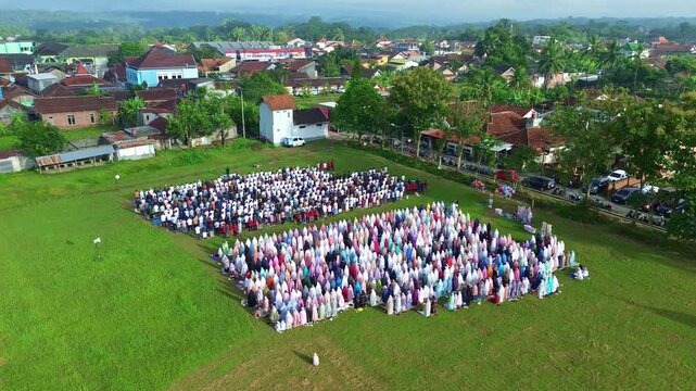 Large outdoor Eid prayer congregation, Muslims praying in rows on green field captured from above.