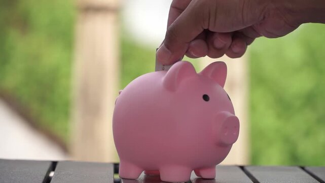 Hand of people inserting coin into piggy bank, symbol of smart saving, budgeting and financial security.