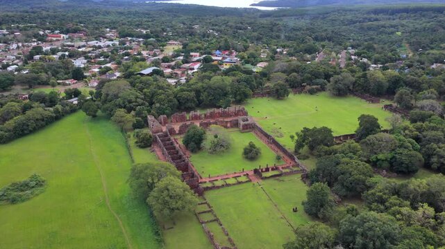 The San Ignacio Mini ruins lie surrounded by greenery and nearby town. Ideal for historical documentaries or travel content.
