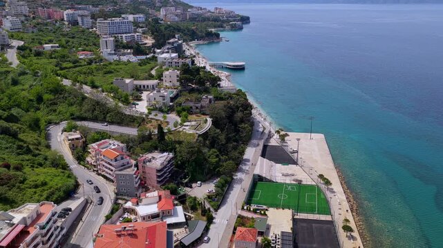 Aerial video over the rugged coastal edge of Vlora, Albania, showcasing the promenade, winding hillside roads, coastal hotels, and the blue Ionian Sea. 