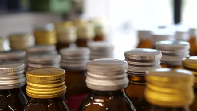 Close up view of numerous small brown glass bottles with silver and gold screw caps, potentially containing syrup or medicine, arranged in rows with a shallow depth of field in a laboratory setting