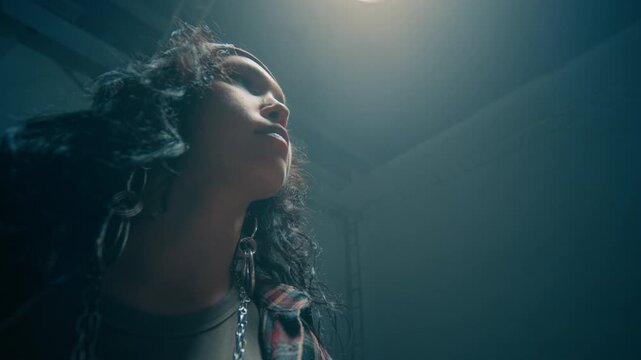 Cinematic low angle shot of camera moving between young man and woman looking at each other with intense stares lit by overhead lighting in dark underground studio