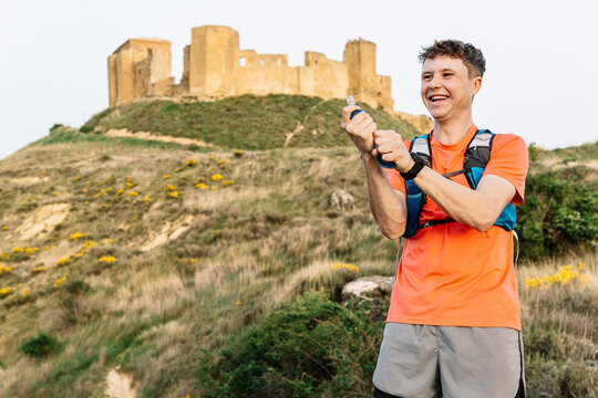 Trail runner hydrating and laughing near ancient castle ruins
