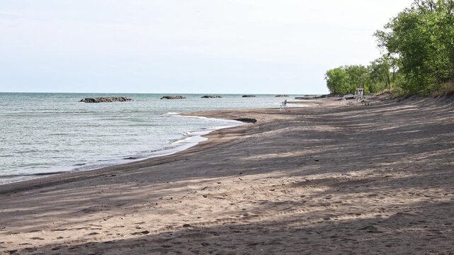 Serene beach Along the shore of Presque Isle State Park, Erie PA,  with gentle waves and trees casting shadows on the sand