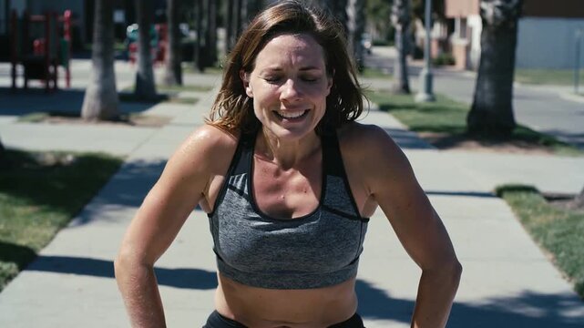 Recovering woman wearing gray sportsbra black shorts steadying, tensing arms on palm-lined sidewalk
