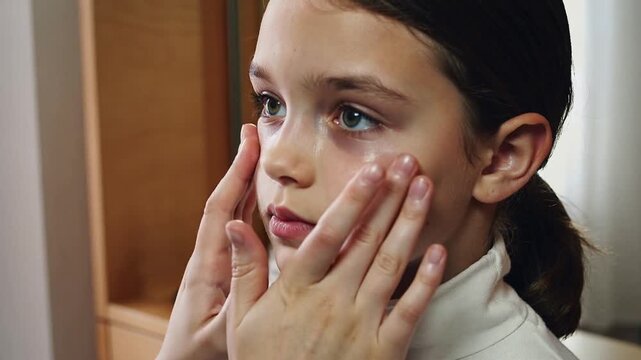Placing adult hands massaging child's tear tracks to soothe face at vanity mirror, pump bottles