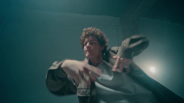 Low angle dynamic urban dance battle scene with camera flowing between young man and woman dancing energetically with cinematic overhead lights in industrial studio