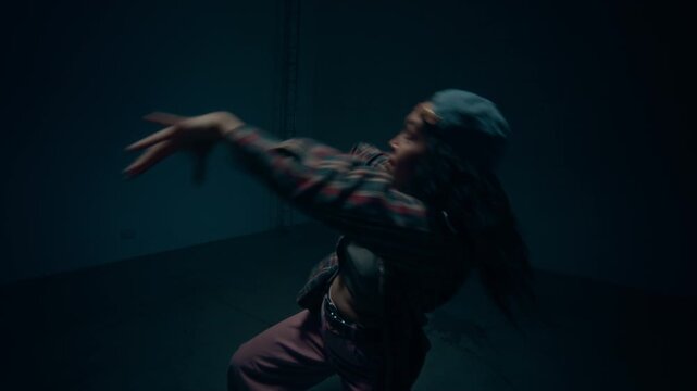 Dynamic shot following young woman performing hip hop freestyle choreography and looking at camera illuminated by moody neon lighting in studio, copy space