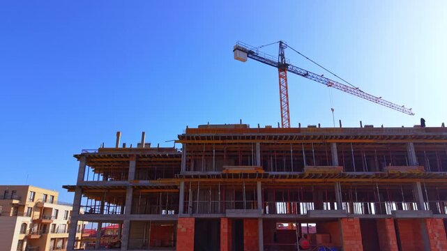 Looking up at a residential structure under development showcasing scaffolding poles and orange brickwork. Aerial view of tower crane above concrete building frame