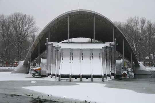 Summer Theater Shell in Lazar Globa Park, Dnipro, Ukraine, January 2009. Frozen lake with thin ice, snow, and swimming ducks in front of the iconic modernist architectural building