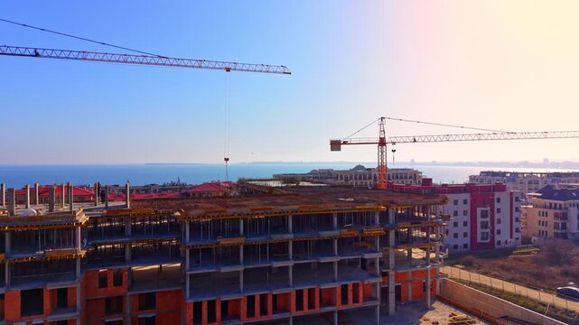 Elevated horizon view of multi level resort housing development with sea and distant shoreline in background. Two tower cranes operating at coastal building site, Bulgaria.