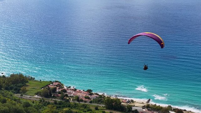Tracking Aerial View of Paragliding Pacarhute Flying Above the sea and the coastline of Tropea, Italy. Summer Activity and Adrenaline Concept, Drone Shot