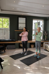 Fototapeta premium Senior women in sportswear practicing yoga with hands in prayer on black mats in living room
