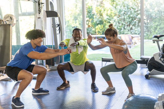 Diverse friends in sportswear performing squats in gym near glass wall with BOSU and weights