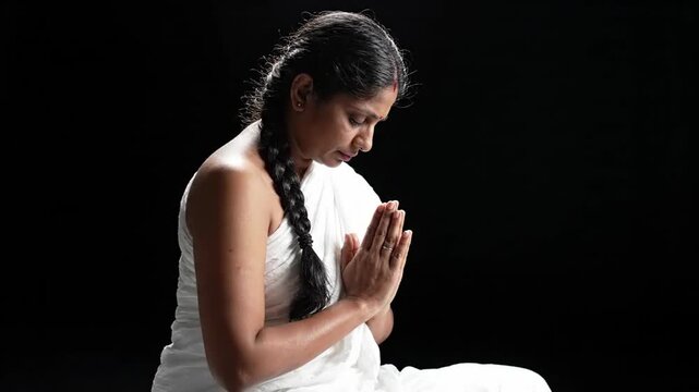 woman in white sari praying with hands together in namaste gesture, serene meditation, spiritual peace, traditional culture, dark background