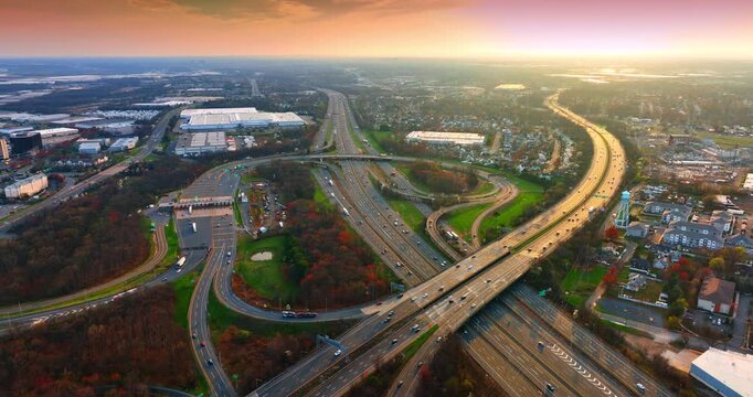 Aerial view of a highway interchange at sunset, New Jersey. Overhead of sweeping ramps and overpasses curving through suburban industrial sprawl beneath a hazy orange sky