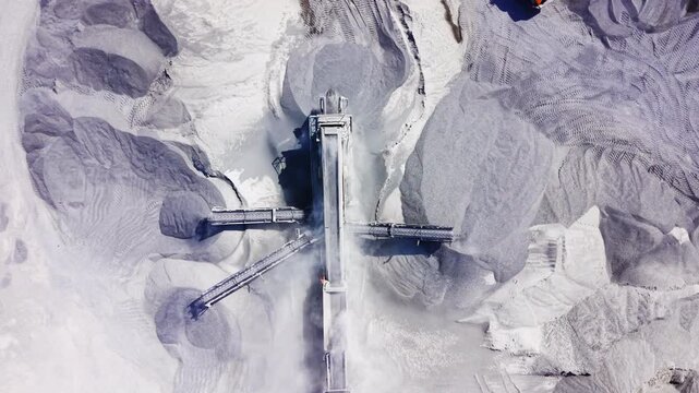 Drone perspective of mechanical sorting machinery shifting aggregate between grey material piles. Abstract top down view of industrial conveyor belt system
