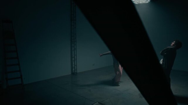 Cinematic wide angle shot of hip hop freestyle dance battle of young man and woman scene shot through metal industrial framing in dark studio, copy space