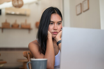 Serious Thai woman propping face with both hands looking at laptop in cafe. © Ranta Images