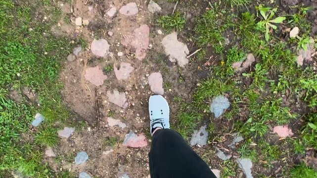 POV of legs walking on different surfaces or rocks, muddy path, grass and asphalt, white shoes, back pants